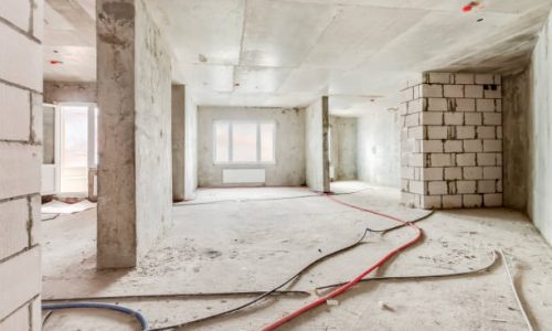 Built structure construction site of residential apartment building. Interior in progress to new house with windows and white brick wall with electric colored wires on the floor.